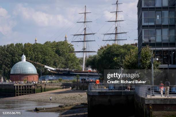 Man walks along the Thames foreshore near the Cutty Sark cargo clipper whose tall masts are seen near the southern entrance of the Greenwich Foot...