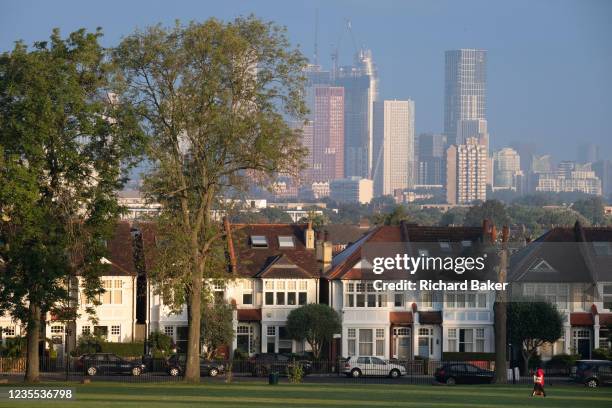 Through a gap of 100 year-old ash trees, Edwardian period homes bordering Ruskin Park in south London with residential high-rises at the distant Nine...