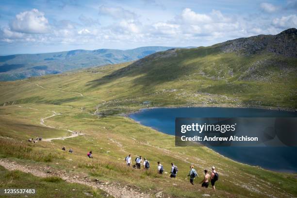 Walkes pass Red Tarn lake high up on the eastern flank of Helvellyn Mountain, English Lake District, Cumbria, United Kingdom on the 2nd of August...