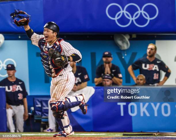 Yokohama, Japan, Saturday, August 7, 2021 - USA players watch from the dugout as Team Japan catcher Takuya Kai joins the celebration winning Gold in...