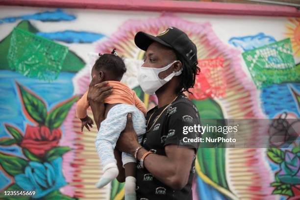 Haitian migrant carries his daughter in front of a mural of the Virgin of Guadalupe inside the Casa de Acogida Formación y Empoderamiento de la Mujer...