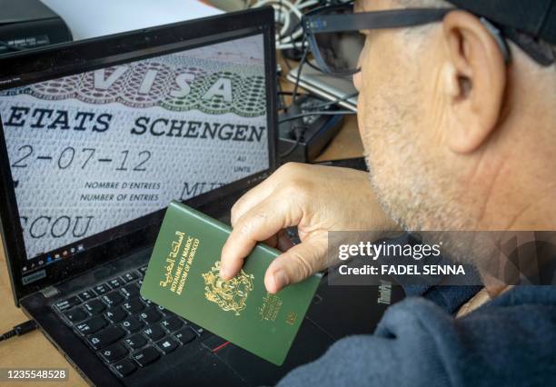 Moroccan man holds his passport in front of his computer displaying a Schengen visa in the capital Rabat, on September 28, 2021. - Paris will sharply...