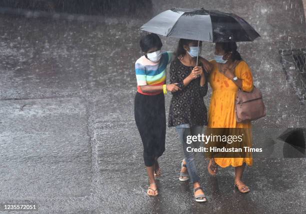 Three girls share one umbrella as they get caught in the sudden downpour of heavy rain at Sion, on September 28, 2021 in Mumbai, India.