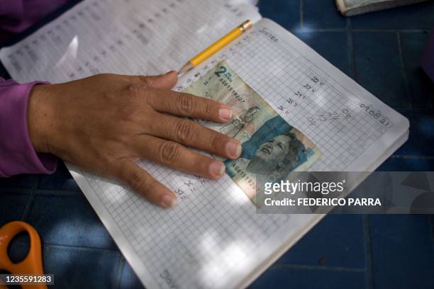 Woman sells lotery tickets outside her house in Puerto Concha town, Zulia state, Venezuela, on September 8, 2021. - Children play with bolivar notes...