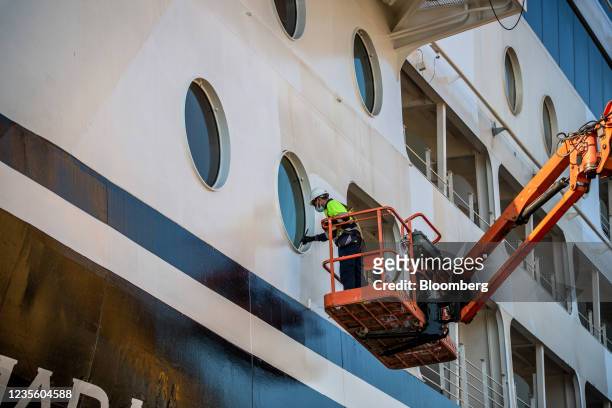 Worker in a cherry picker paints a window frame of the Azamara Journey cruise ship, operated by Azamara Club Cruises, during servicing at the...