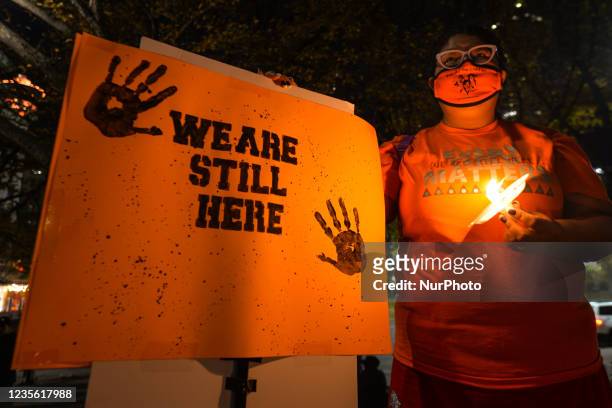 Woman holds a candle and a placard with words 'We Are Still Alive' during a candlelight vigil at the residential school memorial on the steps of...