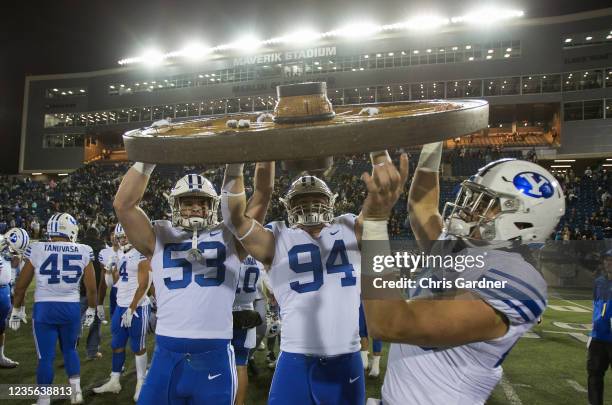 Fisher Jackson, John Nelson, and Payton Wilgar of the BYU Cougars raise the wagon wheel trophy after beating the Utah State Aggies October 1, 2021 at...