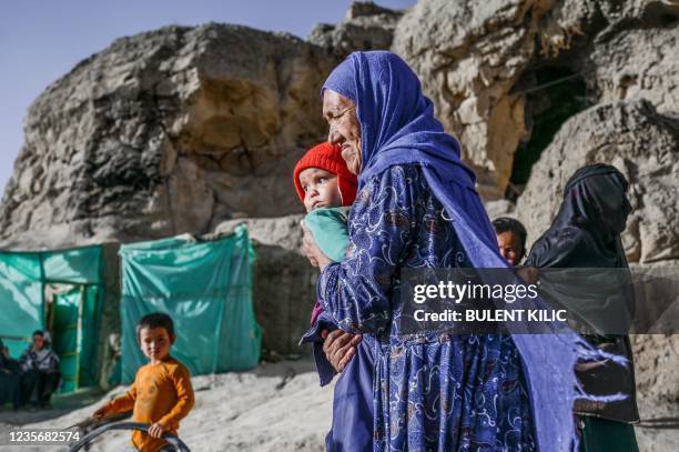 In this picture taken on October 3 a Hazara ethnic woman with a baby walks in front of her cave on a cliff pockmarked by caves where people still...