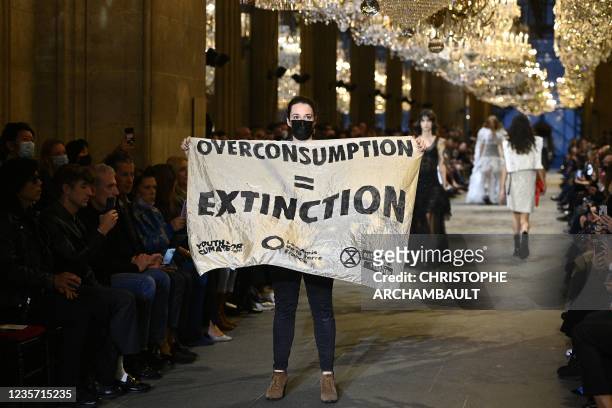 Demonstrator holds a banner as models present creations by Louis Vuitton during the Women's Spring-Summer 2022 Ready-to-Wear collection fashion show...