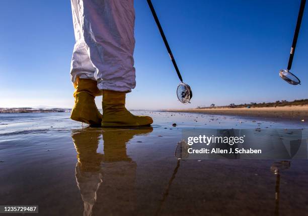 Huntington Beach, CA Environmental oil spill cleanup crews wear protective suits and walk the beach, picking up chunks of oil off the beach from a...