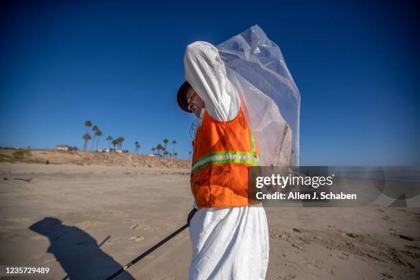 Huntington Beach, CA An environmental oil spill cleanup crew member wears a hot protective suit on a hot day as he walks the beach, loading chunks of...