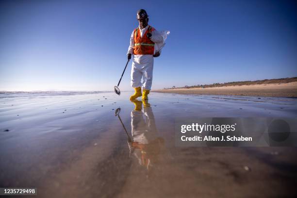 Huntington Beach, CA An environmental oil spill cleanup crew member wears a hot protective suit on a hot day as he walks the beach, loading chunks of...