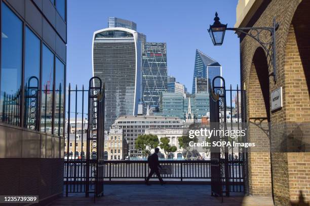 Man walks along Queen's Walk promenade past the City of London skyline on a clear day.