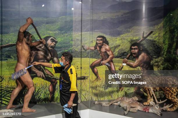 Worker cleans a display with a background infographic about the early men at Bandung Geological Museum . The Bandung City Government provides...