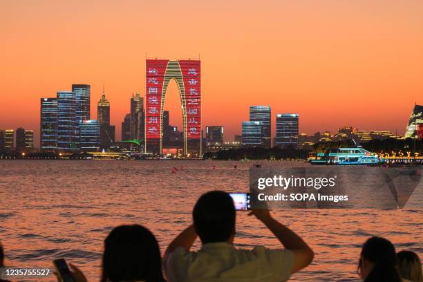 Man takes photos at Suzhou Jinji lake during sunset with the Gate to the East in the background.
