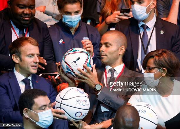 French President Emmanuel Macron and French-US former basketball player Tony Parker sign football balls as they attend a basket-ball game during an...