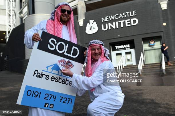 Newcastle United supporters dressed in robes pose with 'sold' placards as they celebrate the sale of the club to a Saudi-led consortium, outside the...
