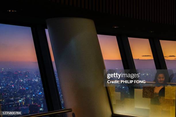 Woman stands at a cafe in Tokyo Skytree as the city skyline is seen at dusk in Tokyo on October 10, 2021.