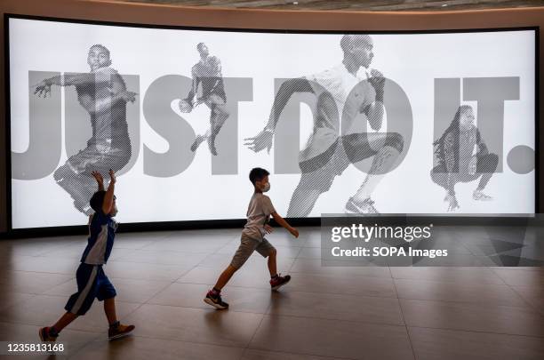 Children play in front of the American multinational sport clothing brand Nike store, logo, with a slogan "Just Do It" illuminated banner in Hong...