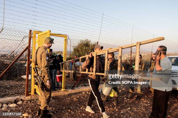 Israeli soldiers are seen guarding the gate of the separation fence as Palestinian farmers make their way to pick olives outside the West Bank city...