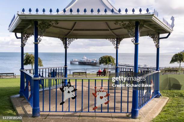 Seen through a modern bandstand that features characters from Alice in Wonderland, a couple sit facing out to see and Llandudno Pier, on 4th October...