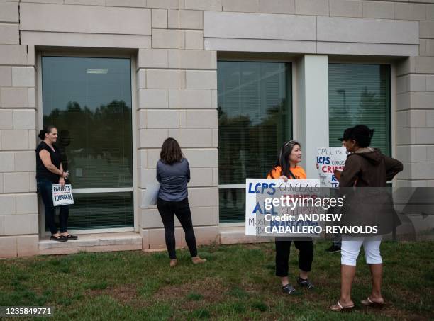 Protesters and activists hold signs as they stand outside a Loudoun County Public Schools board meeting in Ashburn, Virginia on October 12, 2021. -...