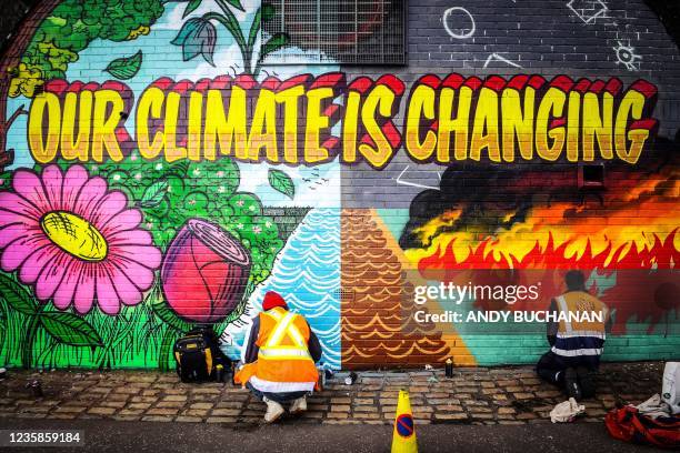 Street artists Ciaran Globel and Conzo Throb paint a mural designed by Colin Li as part of the Grantham Climate Art Prize 2021 on a wall opposite the...