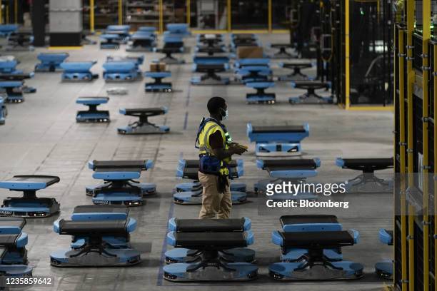 Worker passes robots moving along the floor at the Amazon Air Hub at the Cincinnati/Northern Kentucky International Airport in Hebron, Kentucky,...