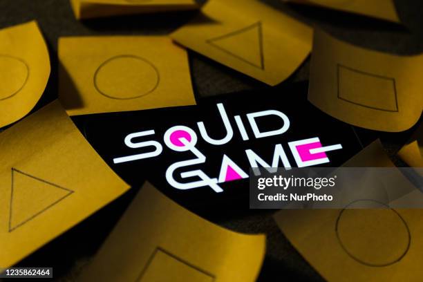 Squid Game series logo displayed on a phone screen and symbols known from the series, drawn on pieces of paper, are seen in this illustration photo...