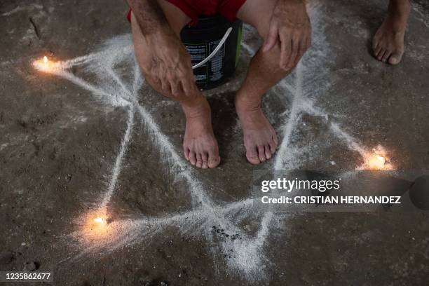 Jose Leandro Mendez sits inside a white star drawn on the pavement and surrounded by candles during a spiritual ceremony for good health after he...