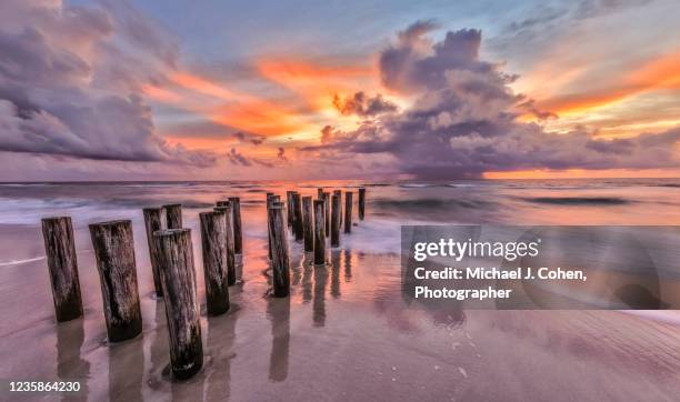 storm, pilings at sunset on the beach. - naples stockfoto's en -beelden