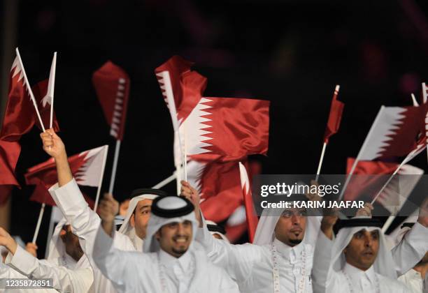 Members of the Qatari team wave national flags during the opening ceremony of the pan-Arab Games in the Gulf emirate's capital Doha on December 9,...