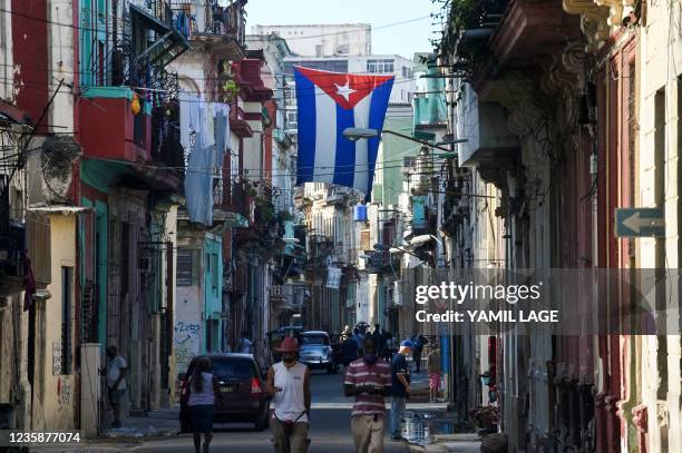 People walk along a street under a Cuban flag, in Havana, on October 14, 2021.