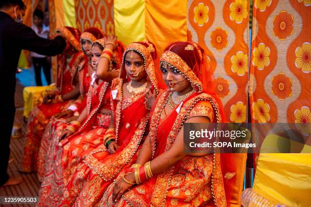 Brides with coy smile in traditional attire sitting together during marriage rituals. Lions Club Delhi Karan organized a samuhik vivah for...