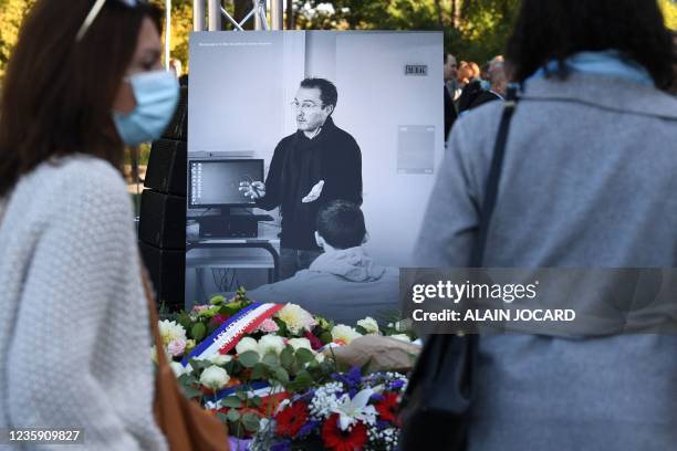 Members of the public stand in front of a photograph depicting French history and geography teacher Samuel Paty as they attend a tribute ceremony in...