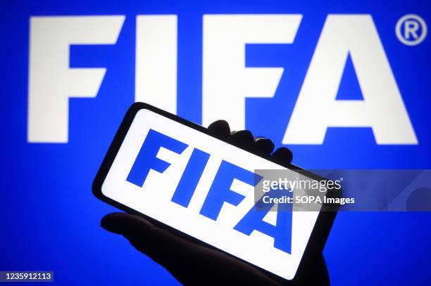 In this photo illustration, FIFA logo is seen on a smartphone in a hand and a pc screen.
