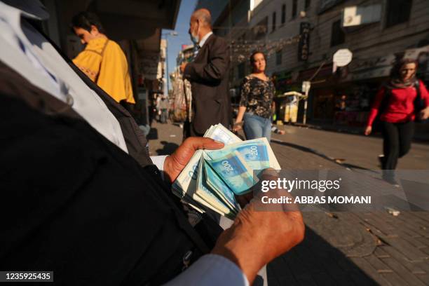 Palestinian man counts a stack of Israeli Shekels in the West Bank city of Ramallah on October 5, 2021. - Palestinian businesses flush with too much...