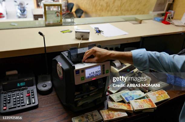 Palestinian man counts stacks of banknotes at a currency exchange counter in the West Bank city of Ramallah on October 5, 2021. - Palestinian...