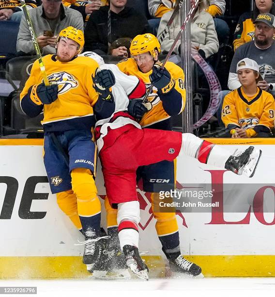 Yakov Trenin and Tanner Jeannot of the Nashville Predators combine for a hit on Tony DeAngelo of the Carolina Hurricanes during an NHL game at...