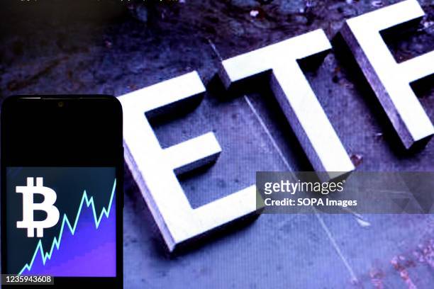 In this Photo illustration a Bitcoin logo seen displayed on a smartphone with an ETF logo in the background.
