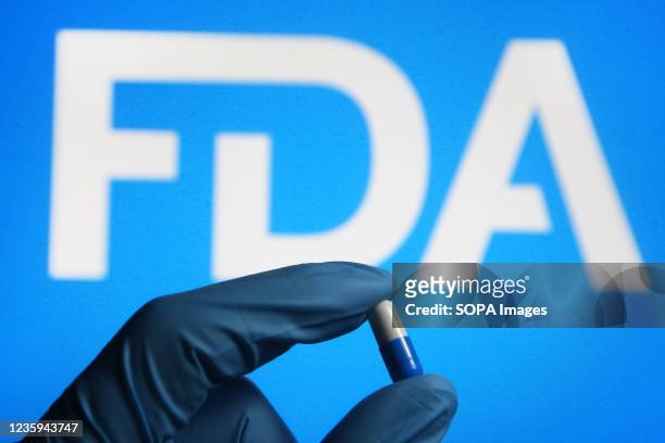 In this photo illustration, a medicine pill is seen in a hand dressed in a medical glove with the U.S. Food and Drug Administration logo in the...