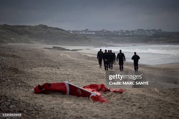 French police officers patrolling the beach between Ambleteusse and Wimereux, northern France, pass by the wreckage of a inflatable boat used by...