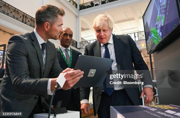 Boris Johnson, U.K. Prime minister, right, looks at a tablet device as he visits the Innovation Zone at the Global Investment Summit 2021 at the...