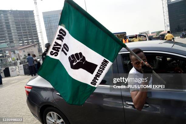 Man in a car carries the Nigerian national flag adorned with writing 'Say No To Oppression' during a protest to commemorate one anniversary of...