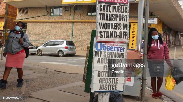 This video grab from an AFPTV video taken on October 19, 2021 in Manzini shows pedestrians walking past posters of newspaper headlines. - Protesters...