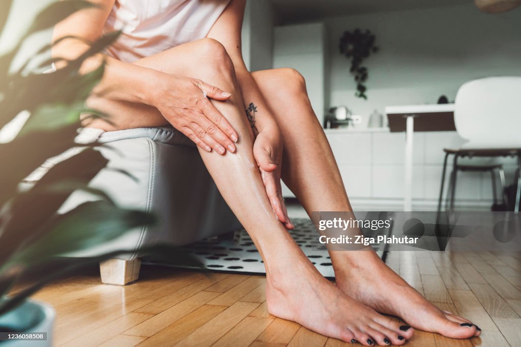 Donna irriconoscibile che massaggia la lozione del corpo sulle gambe