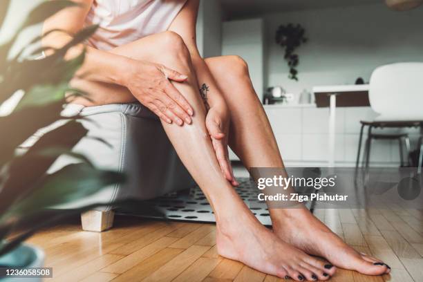 donna irriconoscibile che massaggia la lozione del corpo sulle gambe - mettersi la crema foto e immagini stock