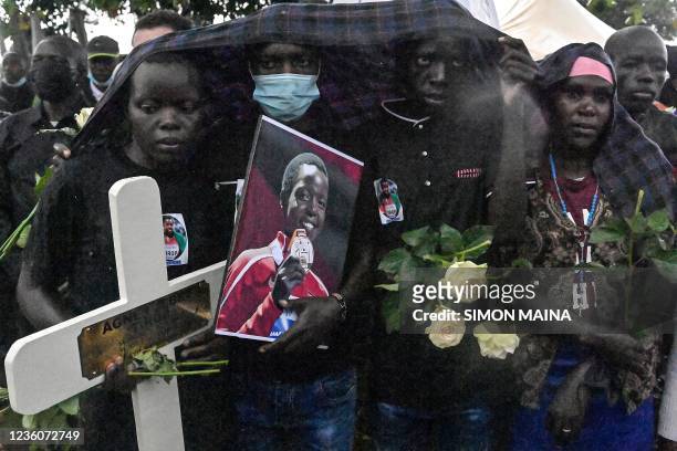 Mourners, holding a portrait photo of Kenyan long-distance runner Agnes Tirop, shield themselves from the rain, during her funerals at Kapnyamisa...