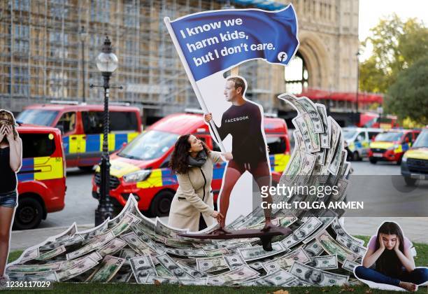 Demonstrator poses with an installation depicting Facebook founder Mark Zuckerberg surfing on a wave of cash and surrounded by distressed teenagers,...