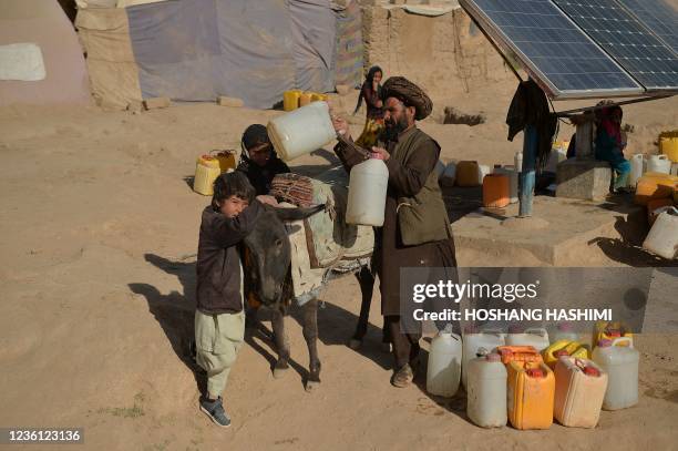 This picture taken on October 17, 2021 shows a man loading a donkey with jerrycans filled with water at the Jar-e-Sakhi Internally Displaced People...